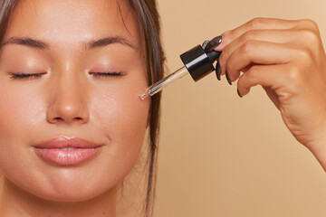Close-up of pretty girl's face moisturizing serum drop onto skin using pipette, skincare product...