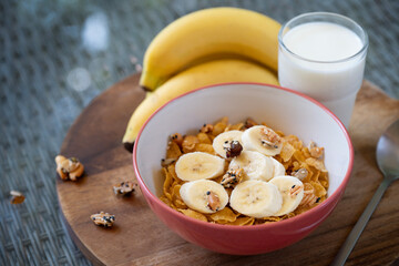 Cornflakes topping with banana and almonds nut for eating with milk or yoghurt in bowl placed on brown placemat. Ready to eat for breakfast or before workout. Healthy food.