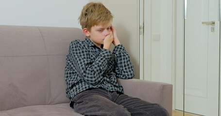 Boy is suffering from toothache sitting on the sofa at home