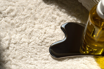 a bottle of oil and a stainless steel gua sha scraper lie on a towel