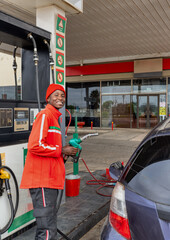 petrol station attendant, african american in red uniform with the nozzle in the hand  refueling a...