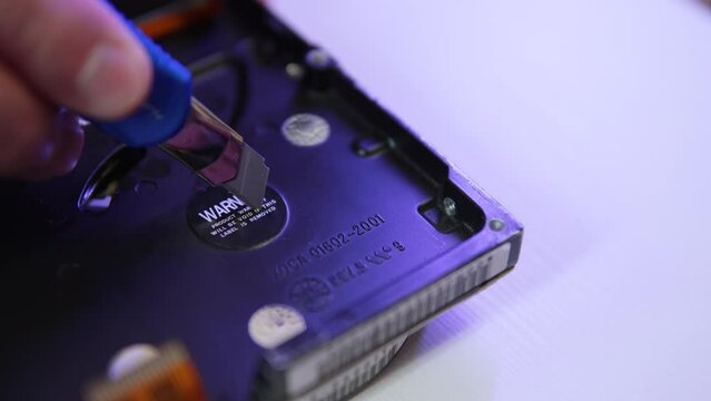 Man cuts off round warranty protection sticker with knife. Repair of complex electronics by master in service center for data recovery. Damage to seals with warning labels indicating loss of warranty.