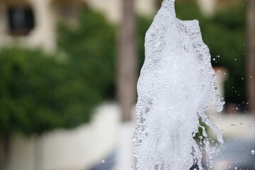 Water fountain geyser caught midair, white water foam frozen in time, foliage in unfocused...