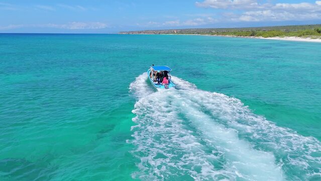 Navigating tourist boat with tourists along Bahia de las Aguilas coastline and shoreline in Dominican Republic. Aerial drone view