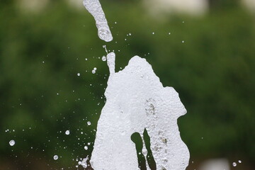 Water fountain geyser caught midair, white water foam frozen in time, foliage in unfocused background