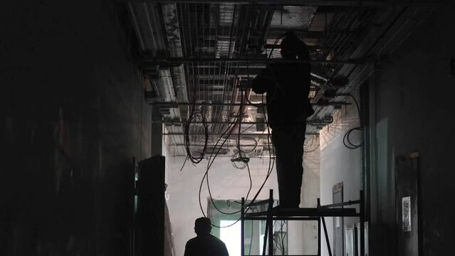 Electrical wiring and cables in a large building. Pipes and cable trays. Construction of infrastructure and management systems. Installers work in a dark room. Construction of an industrial complex
