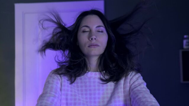 Portrait of a young sleepwalking woman in pajamas slowly raising her hands in front of her at night in a room. Her hair is flying in the air. The concept of somnambulism