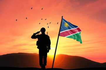 Silhouette of a soldier with the Namibia flag stands against the background of a sunset or sunrise....