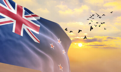 Waving flag of New Zealand against the background of a sunset or sunrise. New Zealand flag for Independence Day. The symbol of the state on wavy fabric.