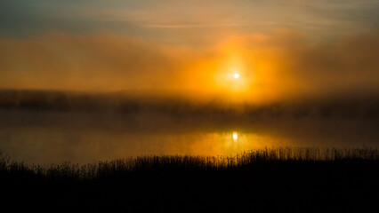 the sun rising over the surface of a lake shrouded in fog