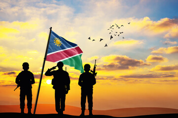 Silhouettes of soldiers with the Namibia flag stand against the background of a sunset or sunrise. Concept of national holidays. Commemoration Day.