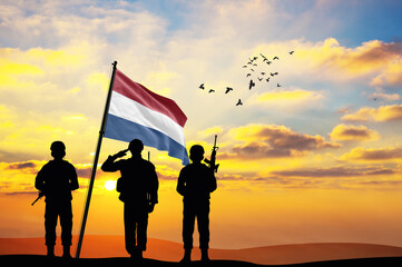 Silhouettes of soldiers with the Netherlands flag stand against the background of a sunset or sunrise. Concept of national holidays. Commemoration Day.