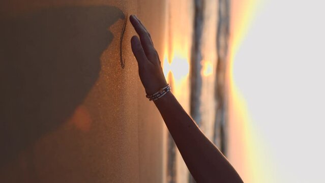 vertical shot. A girl draws on wet coastal sand. a woman's hand runs her fingers through the sand. concept of love and passion.