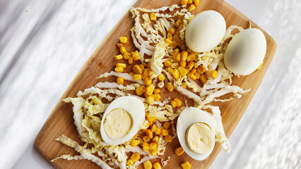 Chopped Peking cabbage, peeled eggs and yellow canned corn on cutting board as a background....
