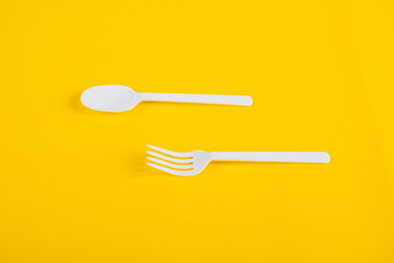 White plastic spoon and fork isolated on yellow background