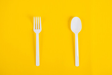 White plastic spoon and fork isolated on yellow background