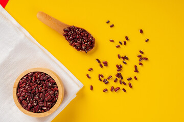 Red kidney beans in wooden cup and wooden spoon on yellow background