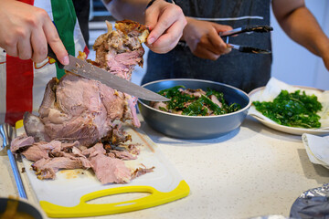 Hands holding a knife and carving a leg of lamb on the kitchen benchtop. Home cooking and...