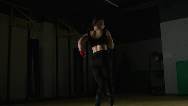 Sporty woman fighter trains his kicks, training in the boxing gym, young woman looks at the camera and trains a series of kicks.