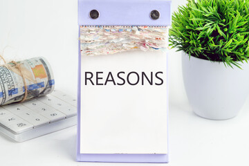 REASONS text, word, inscription on a desktop calendar on a white background next to money and a green flower