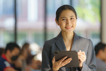 A beautiful Asian businesswoman holding a digital tablet while standing in the office room. Business concept.