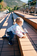 Little girl climbs the steps in the park on all fours with a toy in her hand