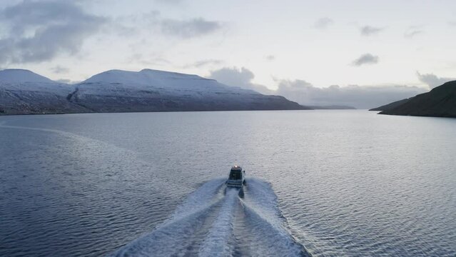 Faroe Islands, 4K Aerial tracking behind fishing boat with snow covered mountains in the background