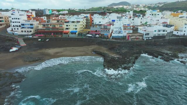 El Puertillo, Arucas, Gran Canaria: Aerial view in orbit over the beach and the houses on the coast. The waves hit the coast hard.