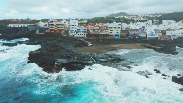 Aerial view in orbit over the beach and houses on the coast of El Puertillo in the north of the island of Gran Canaria and with large waves hitting the coast.