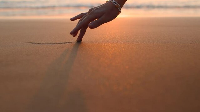 A girl draws on wet coastal sand. beautiful female hands run their fingers through the sand. concept of love and passion.