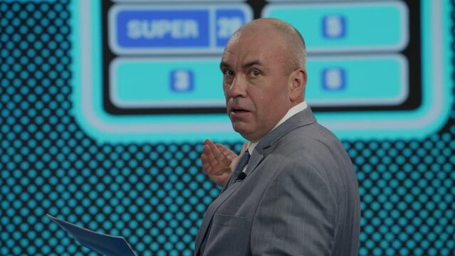 Funny charismatic host talking to the contestants during recording of a fictional morning family game show, guest guessing the right answer