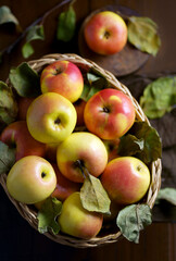 Apples in a basket on a wooden table. Fresh red apples with green leaves on a black background. Fruits. View from above.