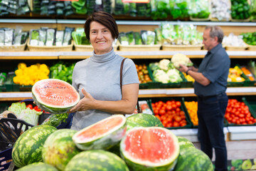 Satisfied woman chooses ripe sweet watermelon on grocery store window