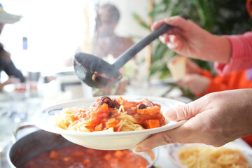 A woman pours a rich tomato sauce onto a plate of steaming pasta, the vibrant colors and textures...