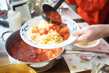 Person pouring tomato sauce on spaghetti 