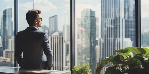 Back View of the Thoughtful Businessman wearing a Suit Standing in His Office, Hands in Pockets and Contemplating Next Big Business Deal, Looking out of the Window. Big City Business District View
 - Powered by Adobe