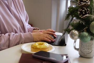 Working online during Christmas. Young cheerful blonde female in warm hoody smiling while chatting with friends using her laptop, sitting in cozy cafe. Winter holidays. Businesswoman, graphic designer