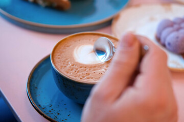 Hand is Mixing the Milk Foam of Latte. Person Stirring Cappuccino with Steel Spoon. Hot Coffee in a...
