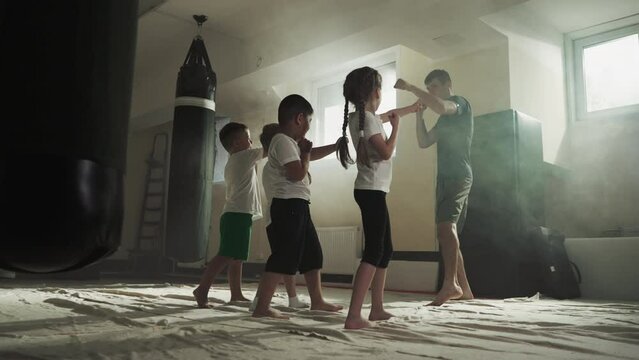 Children do punches with trainer in boxing school