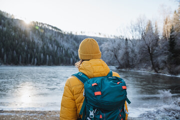 A man admiring a beautiful view of the mountains, a tourist on a winter hike, the glare of the sun over the mountain, a yellow hat on his head, a backpack on his back.