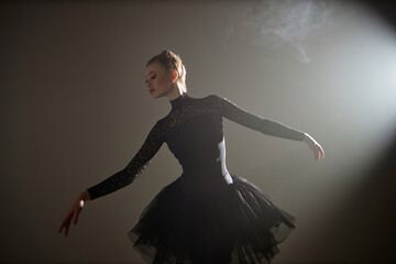 Young caucasian ballerina in black lace dress demonstrating ballet figure in dimly lit studio