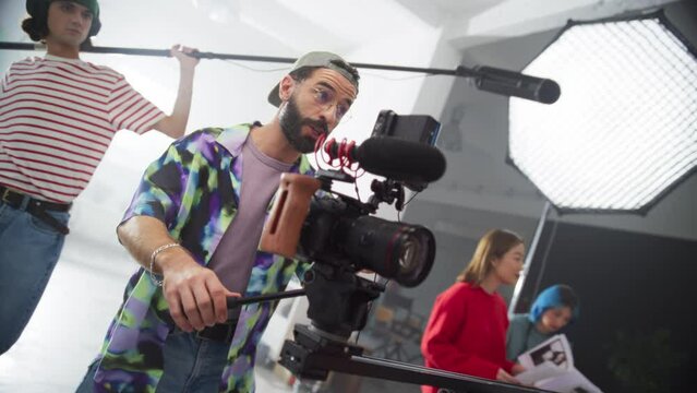 Portrait of Young Videographer Working on Set, Giving Instructions to the Filmed Model. Male Cinematographer Operating an Advanced Digital Camera To Capture High Quality Footage. Slow Motion
