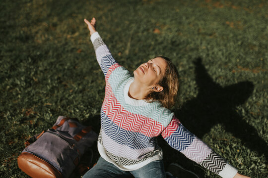 Woman with arms outstretched sitting on grass near backpack