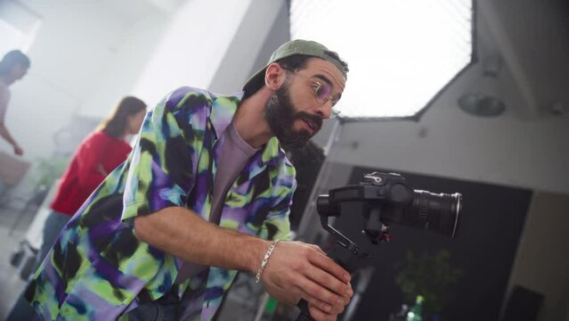 Dynamic Shot of Young Stylish Cinematographer Working on Set: Production Company Crew Filming a Client's Project of a Marketing Campaign. Male Professional Camera Operator Capturing Creative Footage