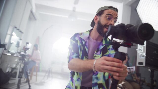 Dynamic Shot of Young Stylish Cinematographer Working on Set: Production Company Crew Filming a Client's Project of a Marketing Campaign. Male Professional Camera Operator Capturing Creative Footage
