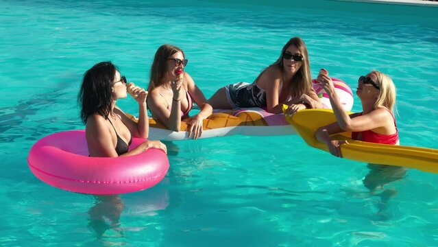 A group of beautiful young women are eating ice cream and having fun in the pool on a sunny summer day. Concept of relaxation, rest and enjoyment