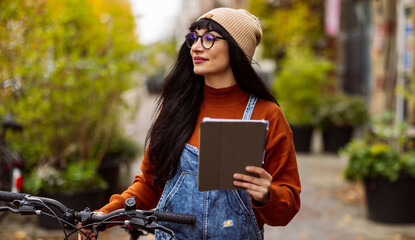 Smiling woman holding tablet PC and standing with bicycle