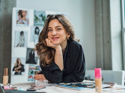 Smiling freelancer sitting with beauty products at desk in studio