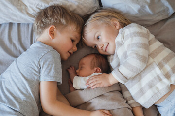 Newborn baby boy sleeping near siblings lying in bed