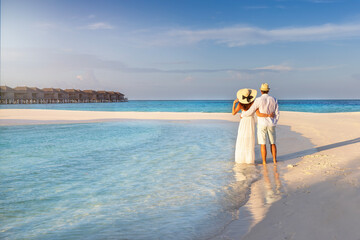 A hugging couple stands on a tropical beach in the Maldives islands and enjoys the sunset view © moofushi